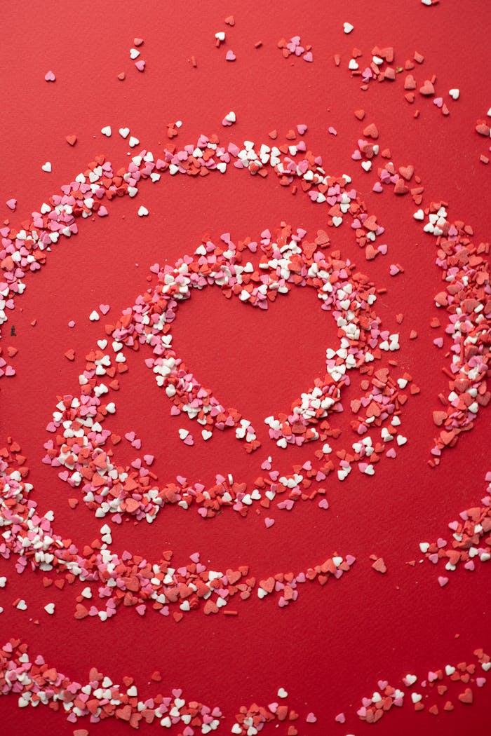 Top view of small confectionery topping scattered on surface and forming heart shape on bright background during saint valentines day celebration